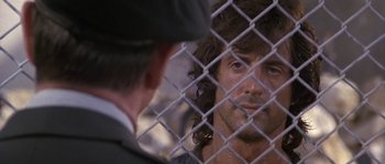 Movie still from “Rambo: First Blood Part II” (1985), directed by George P. Cosmatos – A man looking at himself in the mirror in front of a fence; Close Up shot, Over the shoulder angle