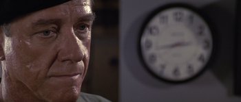 Movie still from “Rambo: First Blood Part II” (1985), directed by George P. Cosmatos – An older man looking at a clock in a room; Close Up shot, Low angle