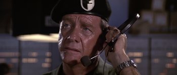 Movie still from “Rambo: First Blood Part II” (1985), directed by George P. Cosmatos – An older man wearing a hat and holding a microphone; Close Up shot, Low angle