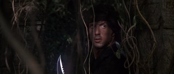 Movie still from “Rambo: First Blood Part II” (1985), directed by George P. Cosmatos – A person holding a knife in a forest; Close Up shot, Low angle