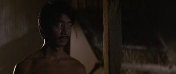 A shirtless man standing next to a wooden pole