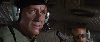 Movie still from “Rambo: First Blood Part II” (1985), directed by George P. Cosmatos – An older man wearing a helmet and holding a gun; Close Up shot, Low angle