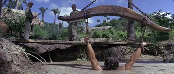 Movie still from “Rambo: First Blood Part II” (1985), directed by George P. Cosmatos – A man standing on a wooden bridge over a body of water; Wide shot, Low angle