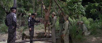 Movie still from “Rambo: First Blood Part II” (1985), directed by George P. Cosmatos – A group of men standing next to each other in the woods; Wide shot, Low angle