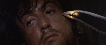 Movie still from “Rambo: First Blood Part II” (1985), directed by George P. Cosmatos – A man's face with a pair of scissors in front of him; Extreme Close Up shot, Low angle