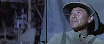 Movie still from “Rambo: First Blood Part II” (1985), directed by George P. Cosmatos – A man with a hat and a backpack under an open umbrella; Close Up shot, Low angle