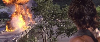 Movie still from “Rambo: First Blood Part II” (1985), directed by George P. Cosmatos – A fire is burning in the background of a tree; Extreme Wide shot, Low angle