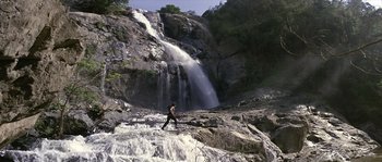 Movie still from “Rambo: First Blood Part II” (1985), directed by George P. Cosmatos – A person walking on a rocky path near a waterfall; Extreme Wide shot, Low angle