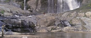 Movie still from “Rambo: First Blood Part II” (1985), directed by George P. Cosmatos – A man sitting on top of a rock near a waterfall; Extreme Wide shot, High angle