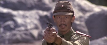 Movie still from “Rambo: First Blood Part II” (1985), directed by George P. Cosmatos – A man holding a gun while standing in front of a rock wall; Close Up shot, Low angle