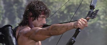 Movie still from “Rambo: First Blood Part II” (1985), directed by George P. Cosmatos – A man is holding a bow and aiming at a target; Close Up shot, Low angle