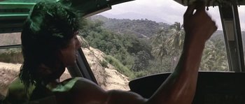 Movie still from “Rambo: First Blood Part II” (1985), directed by George P. Cosmatos – A man driving a car down a mountain road; Medium shot, Over the shoulder angle
