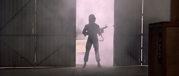 Movie still from “Rambo: First Blood Part II” (1985), directed by George P. Cosmatos – A person holding a gun in a doorway; Wide shot, Low angle