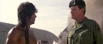 Movie still from “Rambo: First Blood Part II” (1985), directed by George P. Cosmatos – Two men are standing next to each other in the desert; Medium shot, Over the shoulder angle