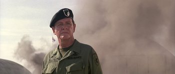 Movie still from “Rambo: First Blood Part II” (1985), directed by George P. Cosmatos – An older man in a military uniform smoking a cigarette in front of smoke; Close Up shot, Low angle