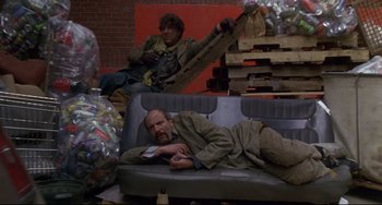Movie still from “Ransom” (1996), directed by Ron Howard – Two men laying down on a couch in a room; Wide shot, Low angle