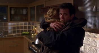 Movie still from “Ransom” (1996), directed by Ron Howard – A man holding a small dog in his arms in a kitchen; Medium shot, Over the shoulder angle