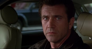 Movie still from “Ransom” (1996), directed by Ron Howard – A person with a car in the background; Close Up shot, Over the shoulder angle