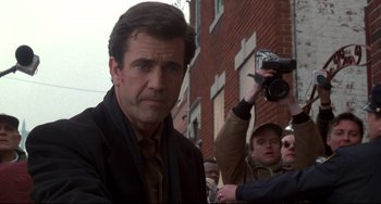 Movie still from “Ransom” (1996), directed by Ron Howard – A man in a black jacket is standing in front of a brick building; Close Up shot, Low angle