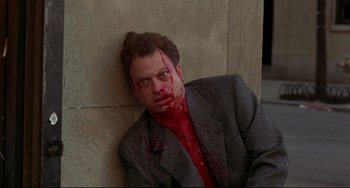 Movie still from “Ransom” (1996), directed by Ron Howard – A man with blood on his face is leaning against a wall; Medium shot, High angle
