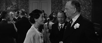 Movie still from “Rapture” (1965), directed by John Guillermin – A group of men and women standing next to each other in a room; Medium shot, Over the shoulder angle