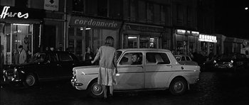 Movie still from “Rapture” (1965), directed by John Guillermin – A woman standing in front of a car on a city street; Medium shot, Over the shoulder angle