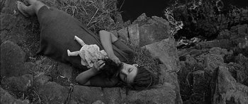 Movie still from “Rapture” (1965), directed by John Guillermin – A young child laying on the ground holding a kitten; Medium shot, Overhead angle