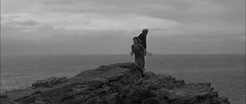 Movie still from “Rapture” (1965), directed by John Guillermin – Two people standing on a rock near the ocean; Wide shot, High angle