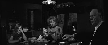 Movie still from “Rapture” (1965), directed by John Guillermin – An older woman sitting at a dinner table with a plate of food in front of her; Medium shot, High angle