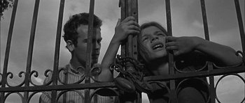 Movie still from “Rapture” (1965), directed by John Guillermin – A man and a woman behind a metal fence; Medium shot, Low angle