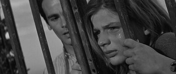 Movie still from “Rapture” (1965), directed by John Guillermin – A man and a woman behind a metal fence; Close Up shot, Low angle