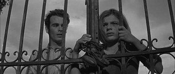 Movie still from “Rapture” (1965), directed by John Guillermin – A man and a woman chained to a metal fence; Medium shot, Low angle
