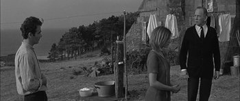 Movie still from “Rapture” (1965), directed by John Guillermin – A woman standing in front of a stone building; Wide shot, Low angle