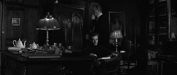 Movie still from “Rapture” (1965), directed by John Guillermin – A man sitting at a desk in front of another man; Medium shot, Low angle