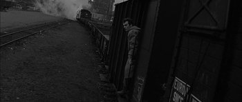 Movie still from “Rapture” (1965), directed by John Guillermin – A man leaning against a wall next to train tracks; Wide shot, High angle
