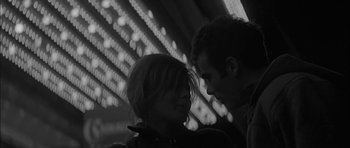 Movie still from “Rapture” (1965), directed by John Guillermin – A man and a woman standing next to each other in front of lights; Close Up shot, Low angle