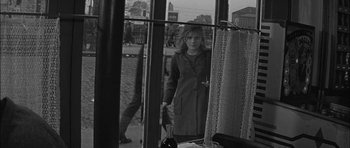 Movie still from “Rapture” (1965), directed by John Guillermin – A black and white photo of a woman standing in front of a window; Medium shot, Over the shoulder angle