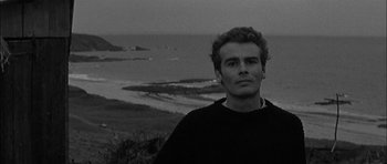 Movie still from “Rapture” (1965), directed by John Guillermin – Black and white photograph of a man in front of the ocean; Close Up shot, High angle