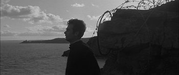 Movie still from “Rapture” (1965), directed by John Guillermin – A black and white photo of a man standing by the water; Close Up shot, Low angle
