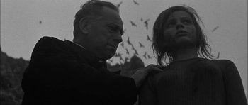 Movie still from “Rapture” (1965), directed by John Guillermin – An older man and a young woman standing next to each other; Medium shot, Low angle