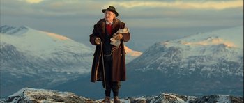 Movie still from “Rare Exports” (2010), directed by Jalmari Helander – An old man standing on top of a mountain holding a dog; Wide shot, Low angle