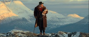 Movie still from “Rare Exports” (2010), directed by Jalmari Helander – An old man standing on top of a mountain holding a dog; Wide shot, Low angle