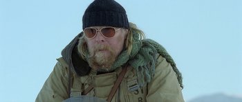 Movie still from “Rare Exports” (2010), directed by Jalmari Helander – A man with a beard wearing sunglasses and a hat; Close Up shot, Over the shoulder angle