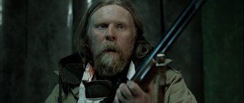 Movie still from “Rare Exports” (2010), directed by Jalmari Helander – A man with a beard holding a rifle; Close Up shot, Low angle