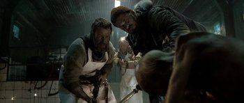 Movie still from “Rare Exports” (2010), directed by Jalmari Helander – A group of people in a room holding tools; Medium shot, Over the shoulder angle