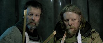 Movie still from “Rare Exports” (2010), directed by Jalmari Helander – Two men with long hair and beards are posing for a picture; Close Up shot, Low angle