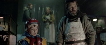 Movie still from “Rare Exports” (2010), directed by Jalmari Helander – A man and a child in a room with other people; Medium shot, Low angle
