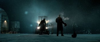 Movie still from “Rare Exports” (2010), directed by Jalmari Helander – A man standing next to a cage in the snow; Wide shot, Low angle