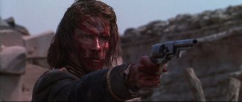 Movie still from “Ravenous” (1999), directed by Antonia Bird – A person holding a gun in a field; Close Up shot, Low angle