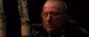 Movie still from “Ravenous” (1999), directed by Antonia Bird – An old man with glasses and a beard; Close Up shot, Over the shoulder angle